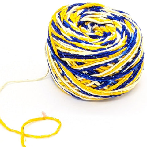 A closeup image of a cake of white, yellow, and blue sparkle worsted weight silk yarn on a white background.