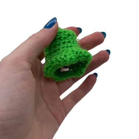A hand holding onto a green crochet bell.