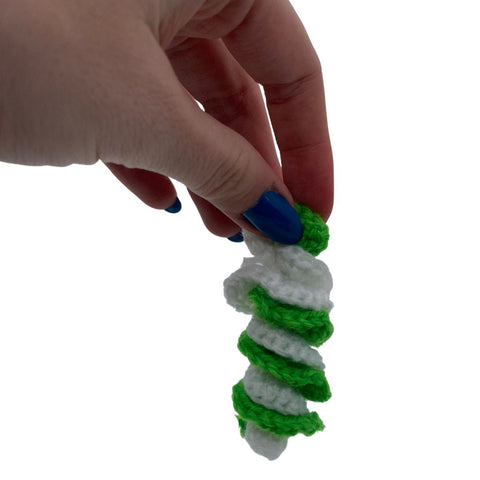 A hand with blue nails dangling a swirling coil made out of made out of green and white yarn