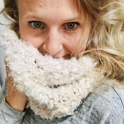 A woman with blonde hair and blue eyes is snuggling into her white cowl.
