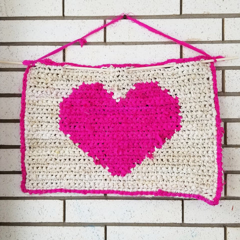 Pink and white all my love wall hanging hung from a white brick wall