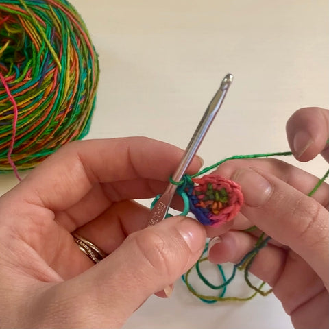 A pair of hands are using a silver crochet hook to crochet the rainbow watercolors lace weight silk yarn