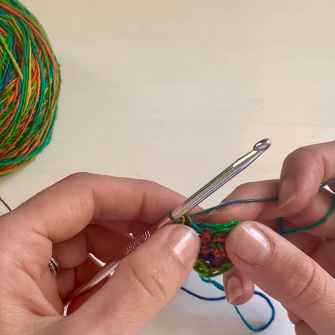 A pair of hands are using a silver crochet hook to crochet the rainbow watercolors lace weight silk yarn