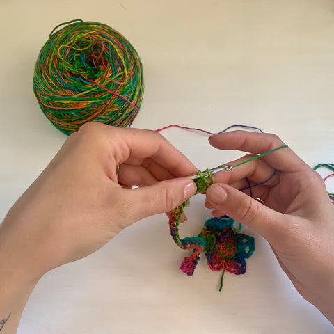 A pair of hands are using a silver crochet hook to crochet the rainbow watercolors lace weight silk yarn