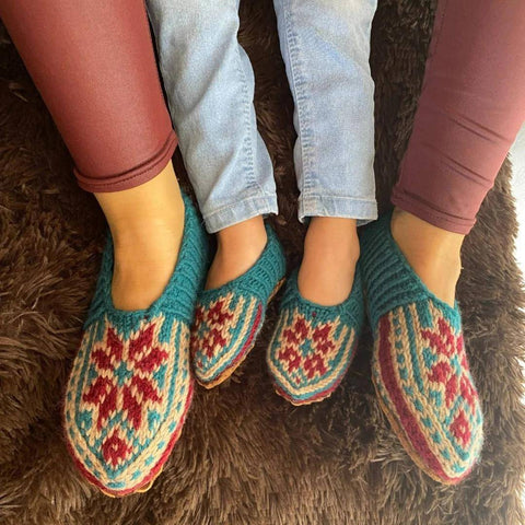 A mother and her child's feet are wearing teal, white, and red handmade slippers on their feet.