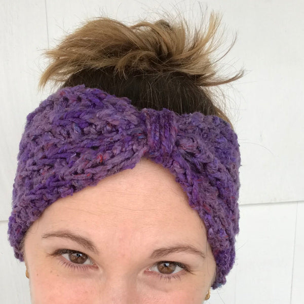 Bow Ear Warmer in purple worn on a woman's head in front of a white background