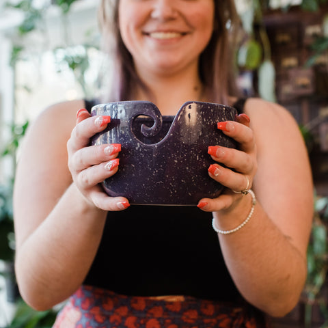 A woman holding up our purple speckled ceramic yarn bowl