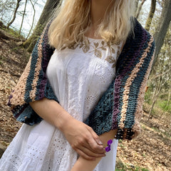 a front side view of designer wearing ebb and flow herbal dyed shrug outside in the autumn woods.