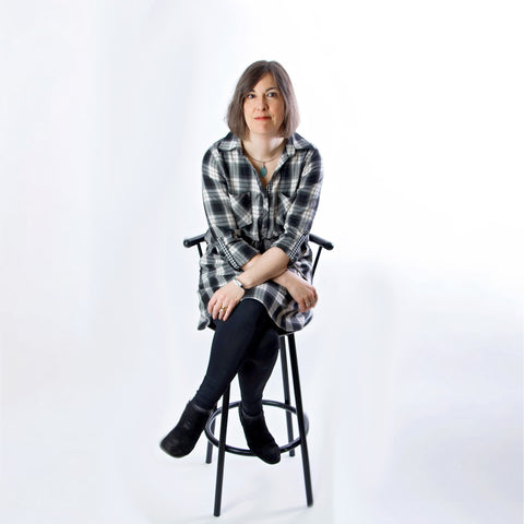 Woman sitting cross-legged on black stool with white background.