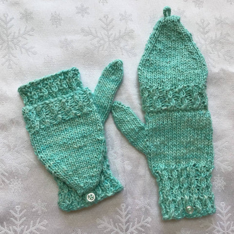 Light green knit mittens in front of snowy white background