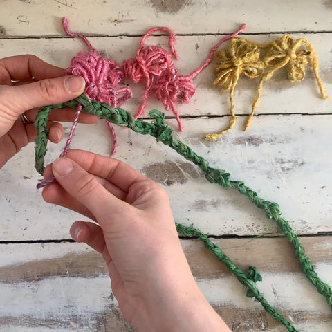 Take one of the puffy fluffy flowers you created, and slide one of the tails left from Step 3 through the lifted braid loop