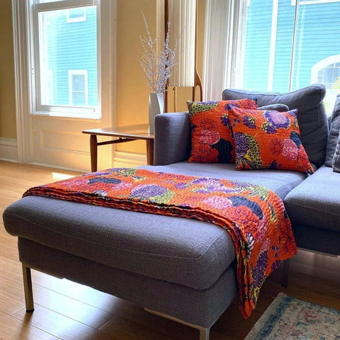 A long grey lounge has an orange pillow and a matching orange quilt thrown over the footrest. 