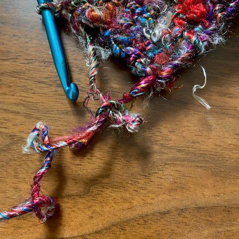 A picture of our Kaleidoscope Banana Fiber yarn on a blue crochet hook. There are a few twists in the working yarn, making it curl up.