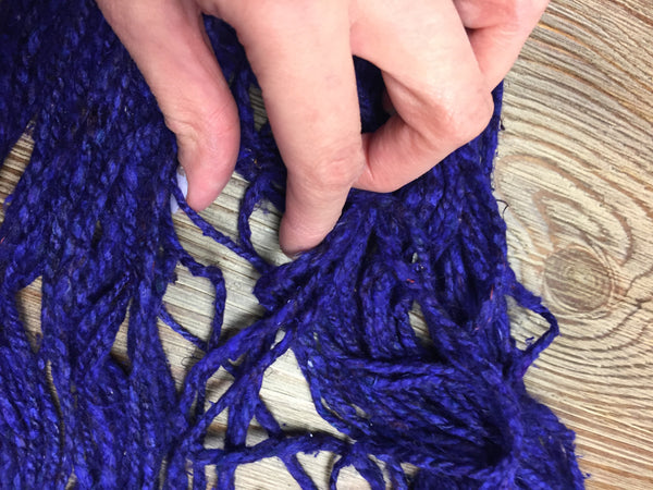 Woman's hand untangling purple yarn over a wooden surface