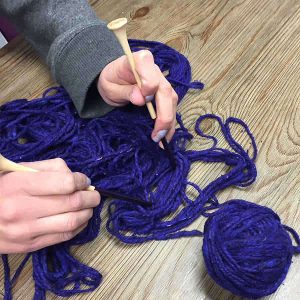 Woman's hands using knitting needles to untangle purple yarn on a wooden surface