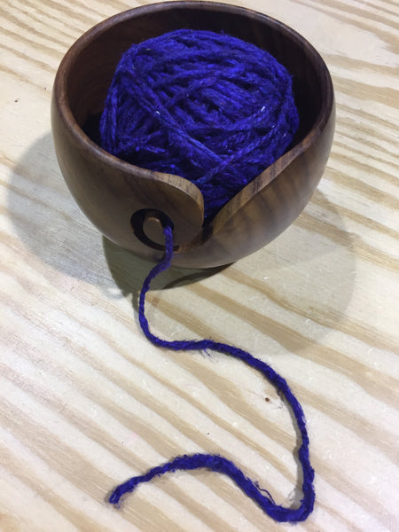 Purple ball of yarn in a wooden yarn bowl on a wooden surface