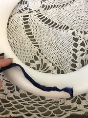 Woman's hand holding blue ribbon over a foam white wreath on top of a white crochet blanket