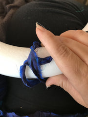 Woman's hand holding blue ribbon over a foam white wreath on top of a black background