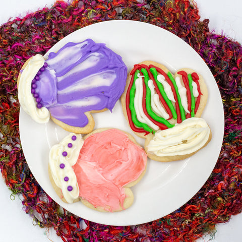 Three frosted sugar cookies on a white plate and knitted coaster