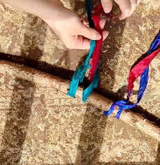 hands tying a piece of sari silk ribbon around a tree branch to make a wall hanging.