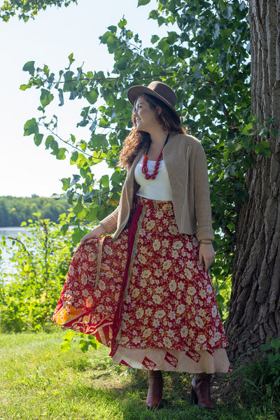 Woman wearing sari wrap skirt, cardigan, and hat in front of a tree