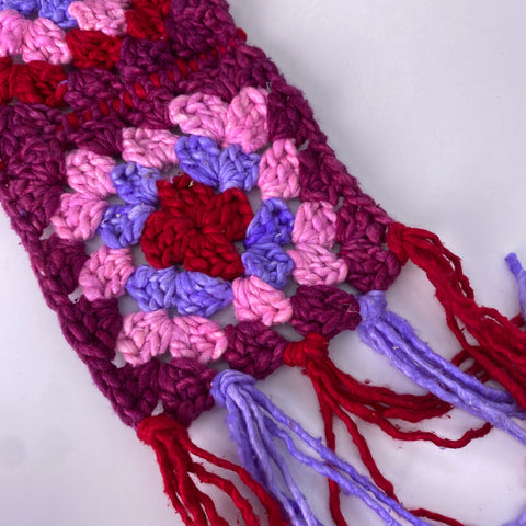 A close up of a pink, red, magenta, and lavender granny square with red and lavender tassels.