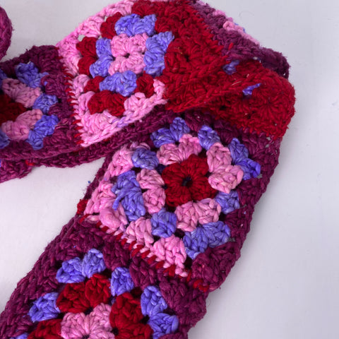 A scarf made of red, pink, magenta, and lavender worsted weight granny squares.