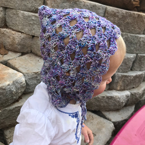 The sideways image of a young baby wearing a pixie bonnet made from blue-purple lace weight silk yarn.