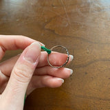 A hand is holding the same silver ring with the yarn now tightly knotted onto the band of the ring.