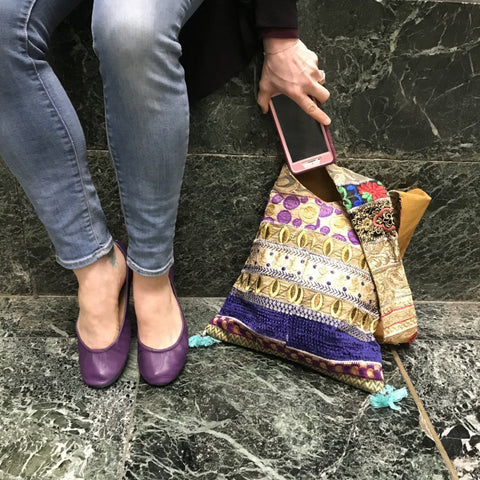 Close up of womans legs standing next to a silk tote bag on the ground next to a stone wall