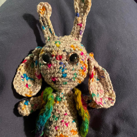 A little alien figure made out of white yarn with multicolored speckles
