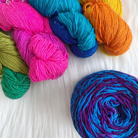 Four different skeins of ombre sport weight yarn, with one ombre blue/purple skein made into a cake.
