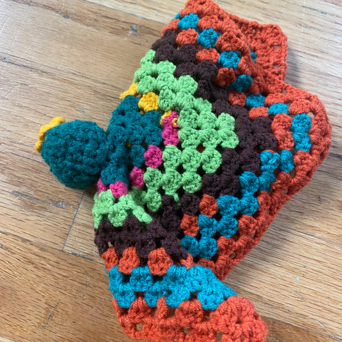The cactus amigurumi snuggle is folded, laying on the wooden floor