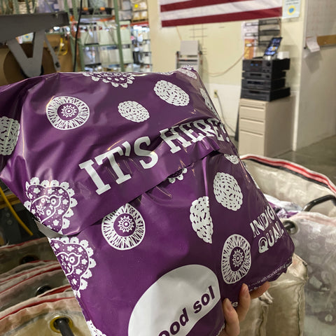 A pretty purple poly mailer from Darn Good Yarn being held up in our warehouse!