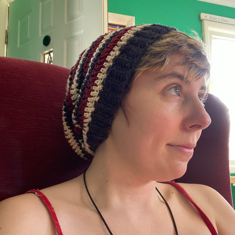 A person with short blond hair wearing a striped black, white, and maroon beanie.