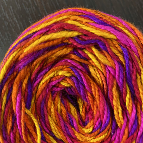 A close up of the autumn jubilee yarn, a handmade silk yarn that is yellow, orange, pink, and purple. 