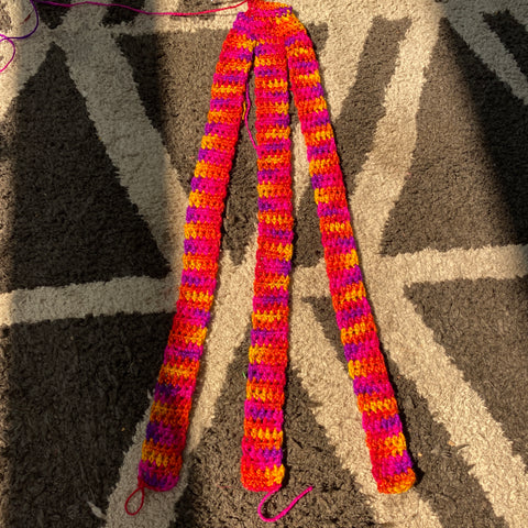 Three strands of crocheted bands are laid out on a white and grey geometric rug in the sun.