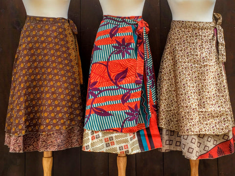 Three mannequins wearing sari wrap skirts in front of a brown wooden wall