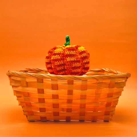 An amigurumi pumpkin on a wicker basket, on an orange background.