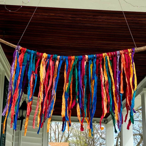 An easy to make DIY rainbow sari silk ribbon wall hanging, hanging on the edge of a porch