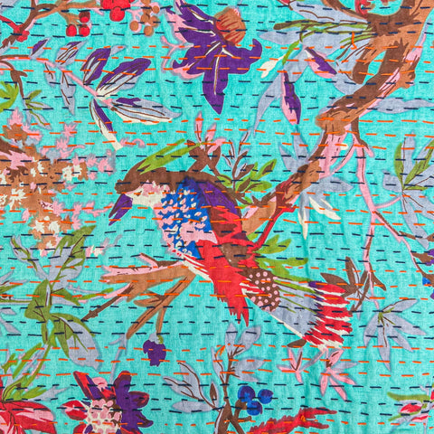 An up close image of a teal piece of handstitched kantha fabric, showing colorful flowers and a bird.