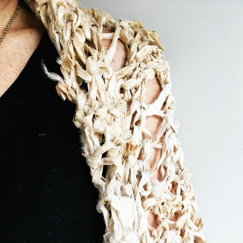 An upclose image of a person's shoulder. They're wearing a black tank top underneath their sari ribbon yarn cocoon coat.