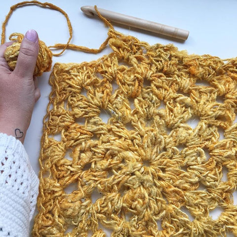 On a white background, the sunny days tank top, made of bright yellow banana fiber is stretched out, a crochet hook still attached to the shirt.