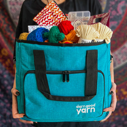 A person wearing a black shirt is holding a teal storage bag, stuffed with yarn and notions