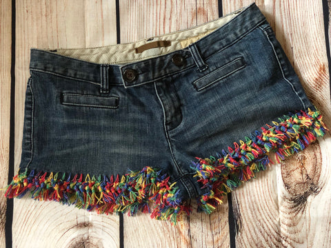 Denim shorts with multicolored crochet fringe sitting on a wooden surface