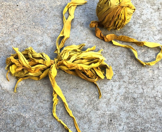 Yellow ribbon tied into a bow next to a yellow yarn ball sitting on a concrete surface