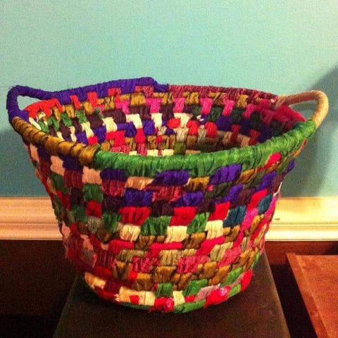 Yarn wrapped rope multicolored basket sitting on a wooden surface next to a turquoise wall