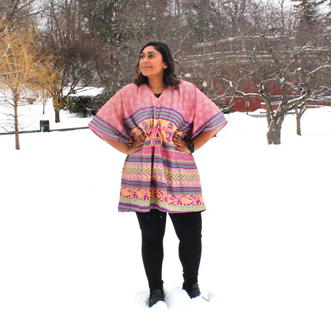 A tan woman with dark hair is standing akimbo out in the snow. She's wearing thick black leggings, black boots, and a pastel pink, purple, and green aanya short tunic