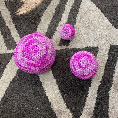 Three balls of spiraled pink yarn have been made via amigurumi crochet techniques and are laying on a geometric grey and white rug