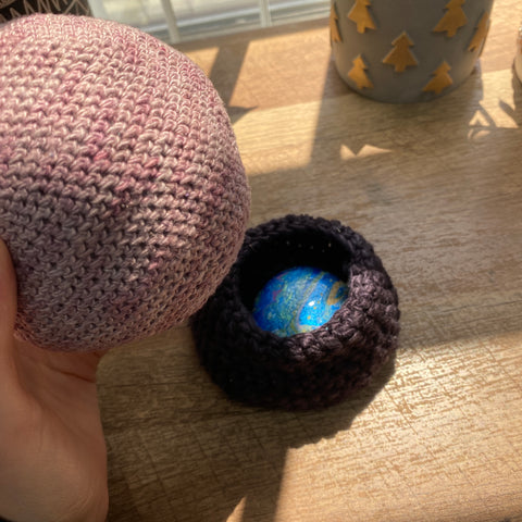 A hand is holding the crystal ball, and beneath is the black base with a shimmering gold and blue painted rock inside the hidden hole.